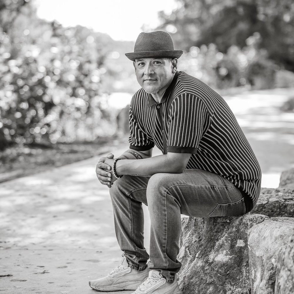 Andy Garcia seated outdoors in a striped shirt and fedora